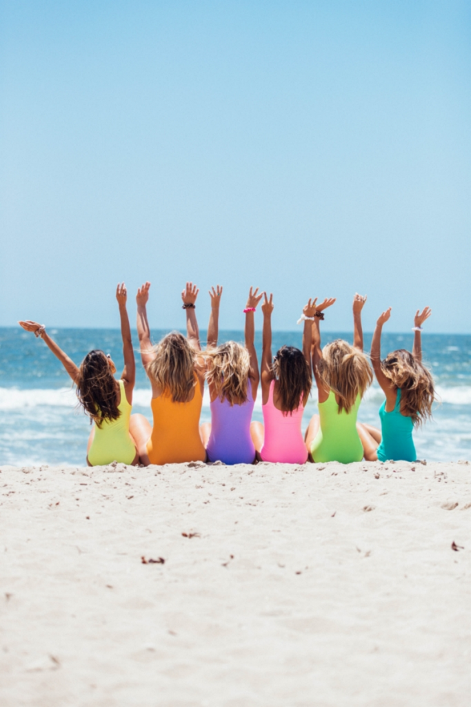 evg evjf 6 filles en maillots de bain de couleur différente installées sur la plage les bras en l'air