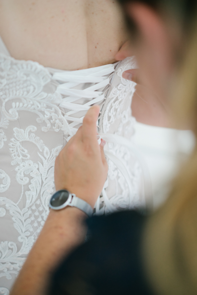 Wedding planner et officiante de cérémonie laïque en train de nouer le laçage de la robe de la future mariée
