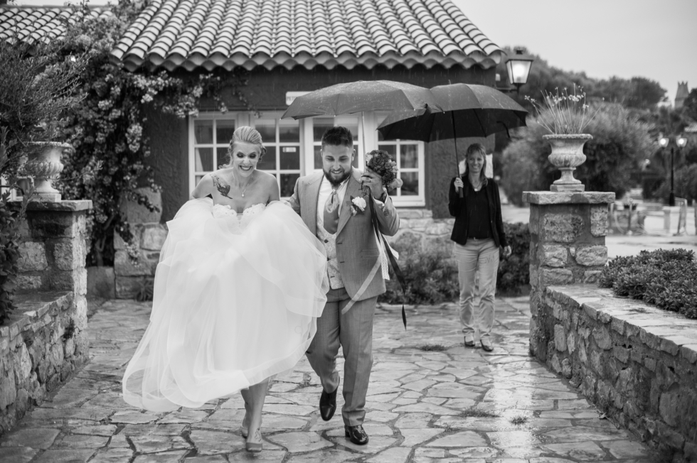 Importance du plan B les mariés en robe et costume courant sous le parapluie pour passer d'un endroit à un autre  ils rigolent