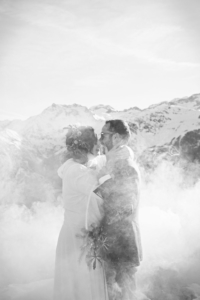 Mariage à la montagne les mariés qui s'embrassent avec la montagne en fond dans la fumée des fumigènes