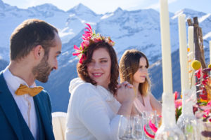 Mariage à la montagne repas avec la table dressée. Chandelles, fleurs colorée et la montagne trône en fond. La mariée regarde son mari
