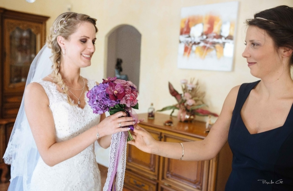 Les romances de MArie donnant le bouquet violet à la mariée en robe blanche et avec son voile