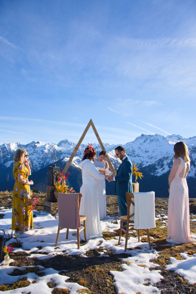 un mariage en hiver : cérémonie laïque devant les montagnes. Le couple de marié au centre avec l'arche triangulaire et l'officiante de cérémonie laïque en fond et les témoind fr chaque côté