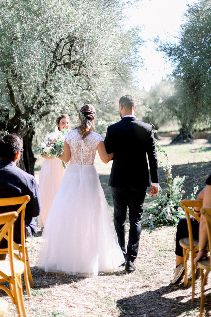 Wedding planner et officiante de cérémonie laïque : arrivée des mariés à la cérémonie laïque avec des oliviers en fond et une arche en flamme 